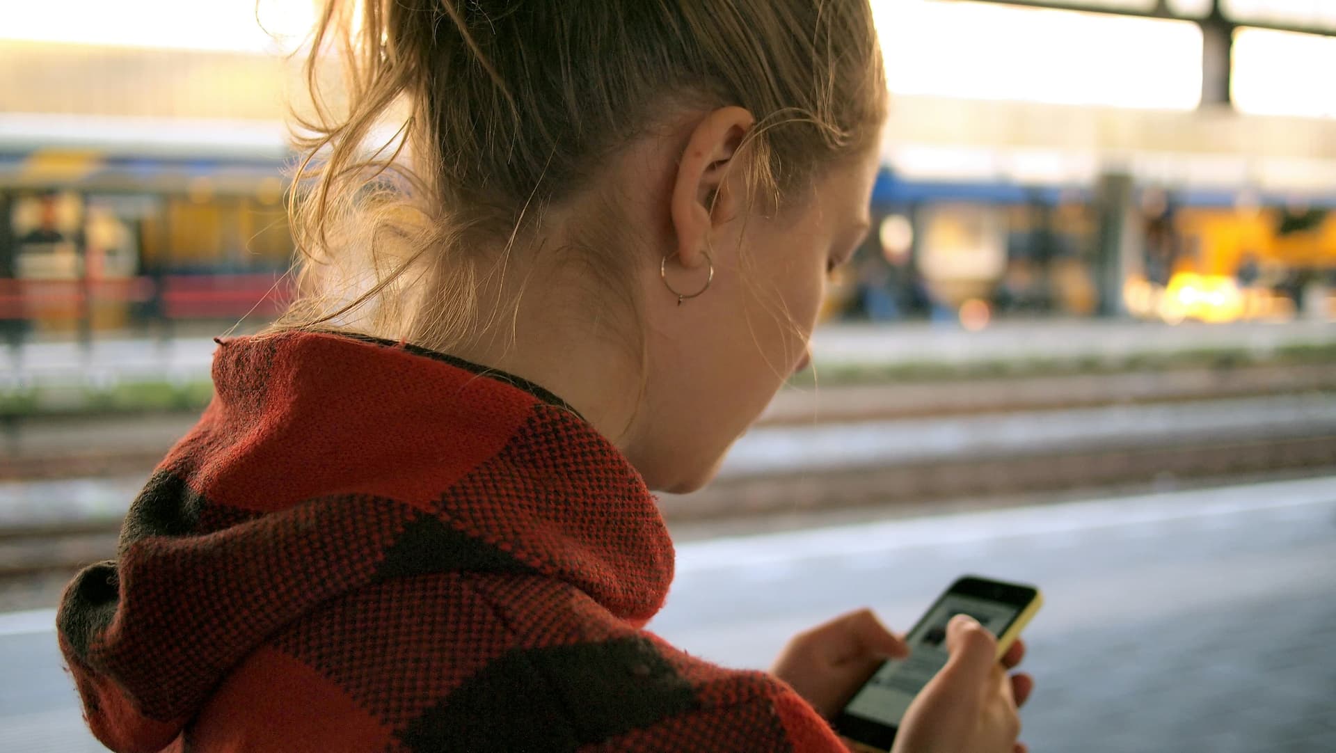 A woman checking her phone while waiting in a bright train station